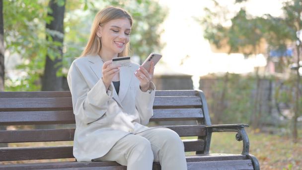 Junge Geschäftsfrau kauft online ein, während sie auf der Bank sitzt - Foto, Bild