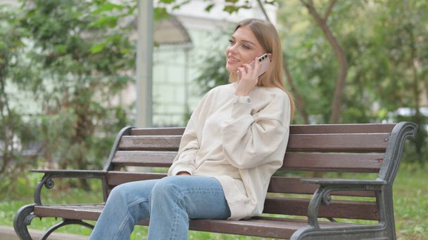 Casual νεαρή γυναίκα μιλάει στο τηλέφωνο, ενώ κάθεται σε ένα μπαλκόνι - Φωτογραφία, εικόνα
