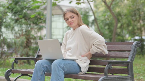 Casual giovane donna utilizzando il computer portatile con mal di schiena mentre seduto all'aperto - Foto, immagini