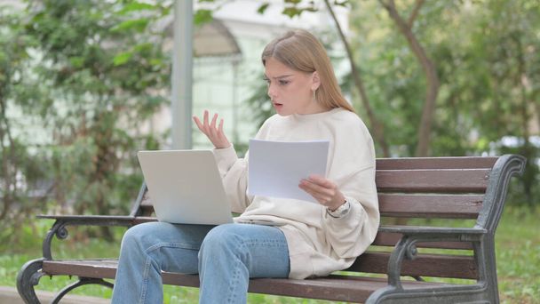 Casual νεαρή γυναίκα αισθάνεται αναστατωμένος, ενώ διαβάζοντας το συμβόλαιο και χρησιμοποιώντας Laptop Εξωτερική - Φωτογραφία, εικόνα