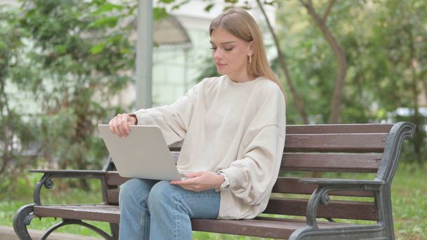 Повседневная девушка приходит, сидит на скамейке и работает на ноутбуке - Фото, изображение