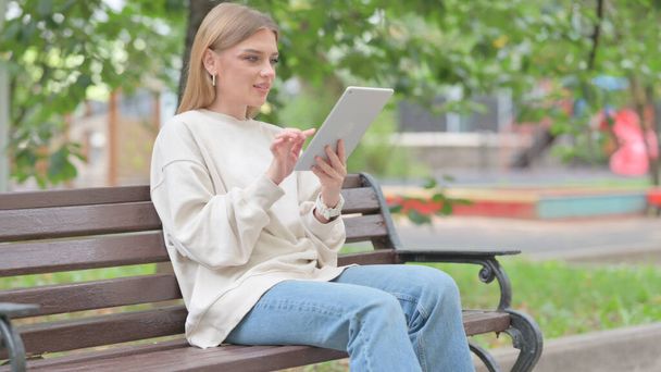 Giovane donna che utilizza Tablet mentre seduto all'aperto su una panchina - Foto, immagini