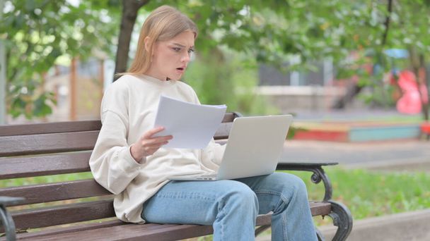 Jeune femme se sentant bouleversé tout en lisant contrat et en utilisant ordinateur portable en plein air - Photo, image
