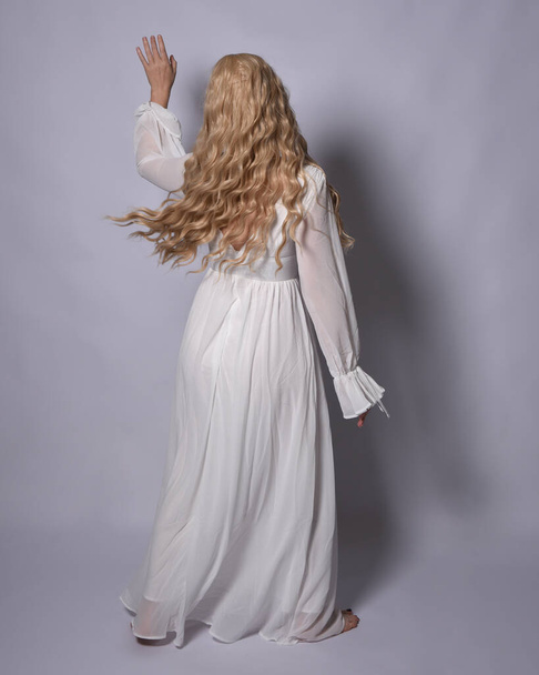 Full length portrait of blonde woman  wearing  white historical bridal gown fantasy costume dress. Standing pose, facing backwards walking away from camera, isolated on studio background. - Photo, image
