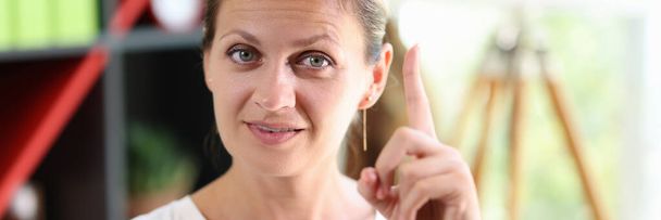 Close-up of shrewd smart woman in casual clothes. Female shows gesture with her index finger up. Symbol of insight and good idea. - Fotoğraf, Görsel