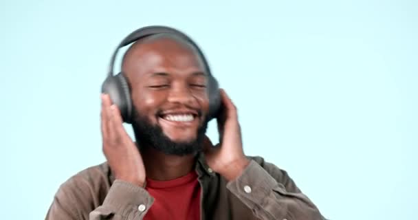 Koptelefoon, dans of vrolijke zwarte man luisteren naar muziek voor de vrijheid in studio op blauwe achtergrond. Glimlach, opgewonden of Afrikaanse persoon die een radiosong, geluid of audio streamt op een online abonnement. - Video
