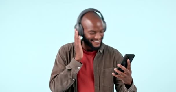 Słuchawki, smartfon lub szczęśliwy czarny człowiek słuchający muzyki dla wolności w studio na niebieskim tle. Uśmiech, wyszukiwanie lub osoba afrykańska streaming piosenki radiowej, dźwięku lub dźwięku w aplikacji mobilnej online. - Materiał filmowy, wideo