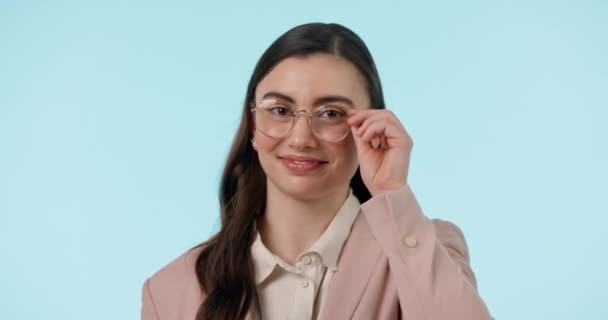 Wink, flirt and face of woman with glasses in studio with confidence, good mood or gesture on blue background. Nerd, portrait and female model with eyeglasses, goofy or silly expression with emoji. - Footage, Video