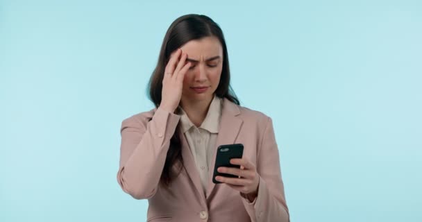 Stress, phone and businesswoman in a studio with headache doing medical research for pain. Frustrated, migraine and professional young female model on a cellphone for telehealth by blue background - Footage, Video