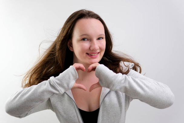 Mosolygó fiatal nő önkéntes mutató kéz jel szív alakú nézi a kamera. Egészséges szív egészségbiztosítás, szeretet és szeretet, önkéntes szociális, szervadományozás koncepció, közeli portré. - Fotó, kép