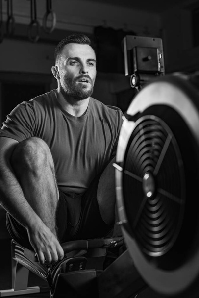 Young man excelling in a rowing machine exercise during cross training, dynamic black and white photo - Photo, Image