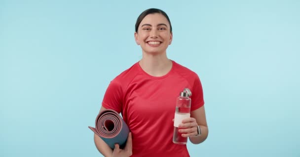 Su şişesi, egzersiz paspası ve egzersiz, sağlık ve sağlık için stüdyoda bir kadın. Spor, susuzluk ve yer ile antrenman için mavi arka planda bulunan mutlu genç kadın portresi. - Video, Çekim