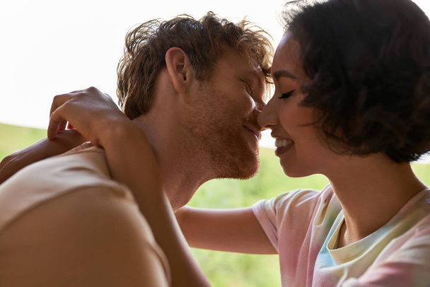 vue rapprochée du couple interracial heureux embrasser et sourire à la maison, coller et tendresse - Photo, image