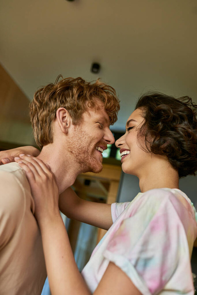 side view of happy interracial couple looking at each other and laughing, having a good time - Foto, afbeelding
