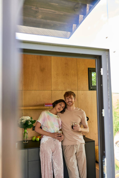 gyönyörű multietnikus pár áll pizsamában, és a kezében csésze reggeli kávé a konyhában - Fotó, kép