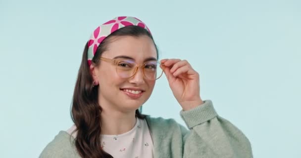Face, wink and woman with glasses, style and confident hipster on a blue studio background. Portrait, happy person and model with eyewear, flirty and looking with aesthetic, stylish and clear vision. - Video, Çekim