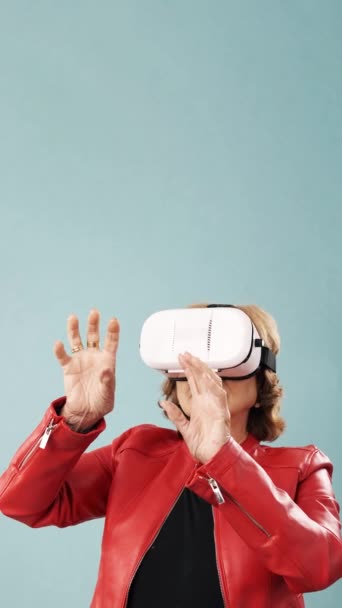 Üst düzey kadın, mavi arka planda dikilirken sanal gerçekliği VR gözlükleriyle yaşıyor. Teknoloji ve yenilik kavramı. - Video, Çekim