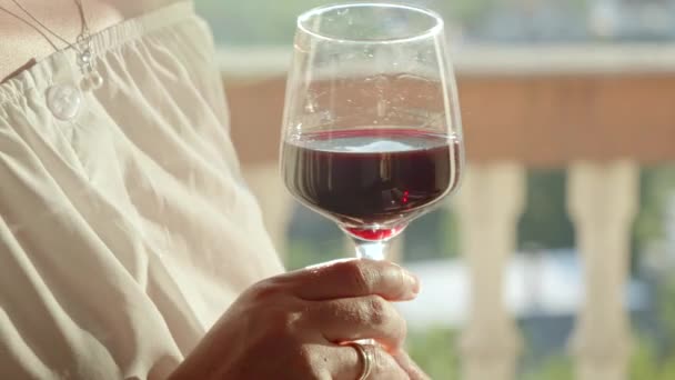 Close-up van de vrouw die rode wijn in glas roert terwijl ze op het balkon of terras van de villa staat. - Video