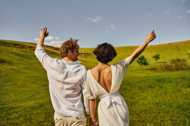 wiejskie wesele, panna młoda w sukni ślubnej trzymająca się za ręce ze szczęśliwym panem młodym na polu, para małżeńska - Zdjęcie, obraz