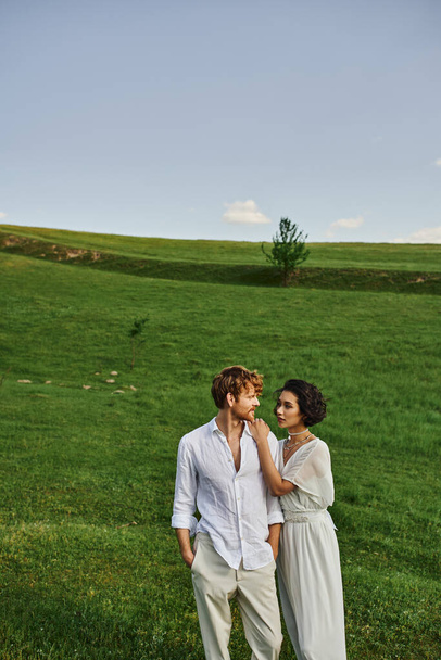just married multiethnic couple standing together in green field, scenic and tranquil landscape - Photo, Image