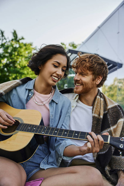 joyful asian woman playing acoustic guitar to happy boyfriend near glass house in countryside - 写真・画像