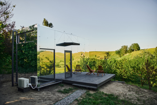 μοντέρνο μινιμαλιστικό γυάλινο σπίτι με καρέκλες και τραπεζάκι στη βεράντα, ήσυχο και γραφικό περιβάλλον - Φωτογραφία, εικόνα