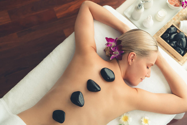 Panorama top view hot stone massage at spa salon in luxury resort with day light serenity ambient, blissful woman customer enjoying spa basalt stone massage glide over body. Quiescent - Photo, Image