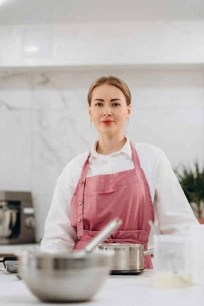 Beautiful young brunette pastry chef woman cooking pastries at the kitchen smiling cheerful presenting and pointing with palm of hand looking at the camera. . High quality photo - Foto, Bild