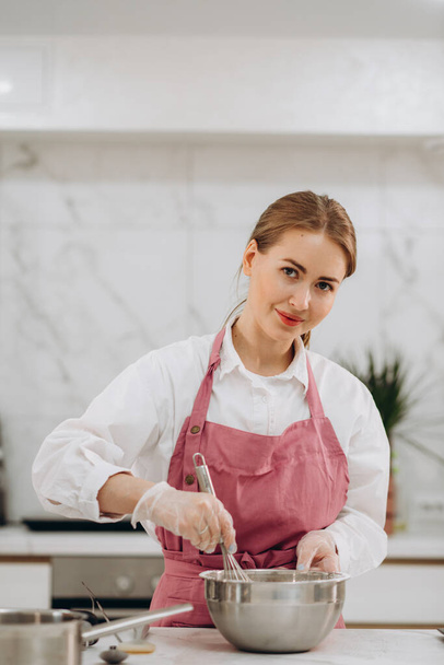 Boldog fiatal szakács lány visel kötényt, használja a mobiltelefon az otthoni konyhában sütés közben pite, pizza, sütemény, fotózás nyers pékség élelmiszer blog, csevegés, hogy hívja. Kiváló minőségű fénykép - Fotó, kép
