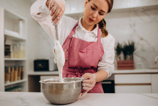 La joven pastelera añade pasta de pistacho al jarabe hirviendo. Cocinar el postre en una cocina profesional. Foto de alta calidad - Foto, Imagen