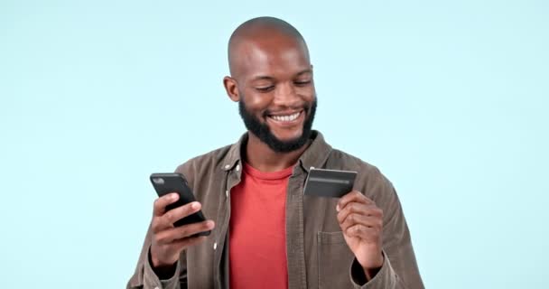 Phone, credit card and black man online shopping in studio isolated on blue background mockup space. Smartphone, ecommerce and happy customer on plastic money in banking, internet finance and payment. - Footage, Video