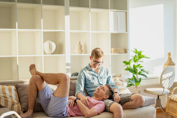 Young happy cute gay couple spending time in a modern apartment talking on the sofa. LGBT family - Foto, Imagem