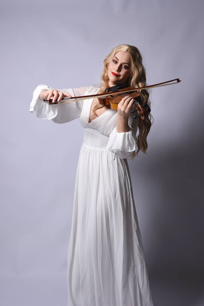 Close up portrait of beautiful blonde model wearing elegant  white halloween gown, a historical fantasy character.  Holding a violin musical instrument, isolated on studio background. - Photo, Image