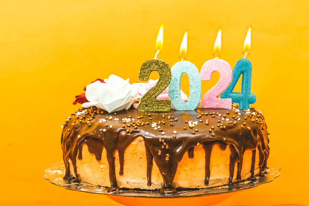 2024 nouvelle année gâteau d'anniversaire chocolat et crème décorée de chiffres bougie et fleurs - Photo, image