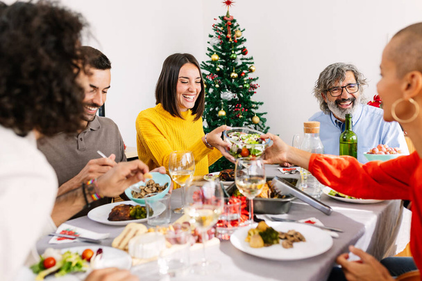 Feliz familia multigeneracional disfrutando de la cena de Navidad en casa. Gran grupo de diversas personas que se divierten juntos celebrando Navidad se reunieron alrededor de la mesa de comedor. - Foto, imagen