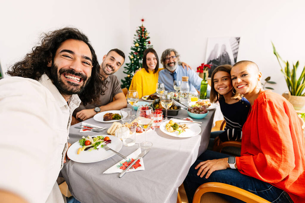 Feliz família multi-geracional tomando selfie retrato juntos sentados na mesa no jantar celebração de Natal - Foto, Imagem