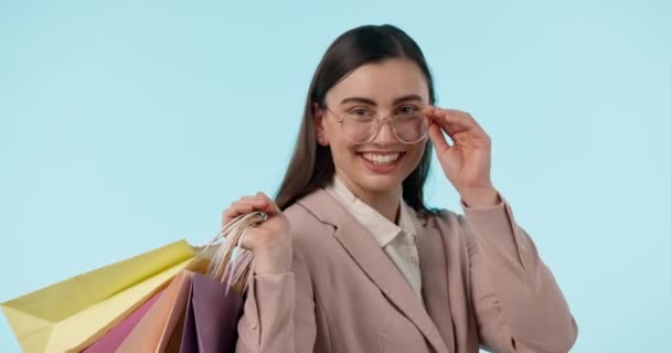 Yüzü, gözlükleri ve alışveriş çantası olan mutlu bir kadın mavi arka planda izole edilmiş. Moda portresi, müşteri gülümsemesi ve indirimli hediyeler, indirimli satışlar ve butikte, alışveriş merkezinde ve perakende mağazasında satın alma - Video, Çekim