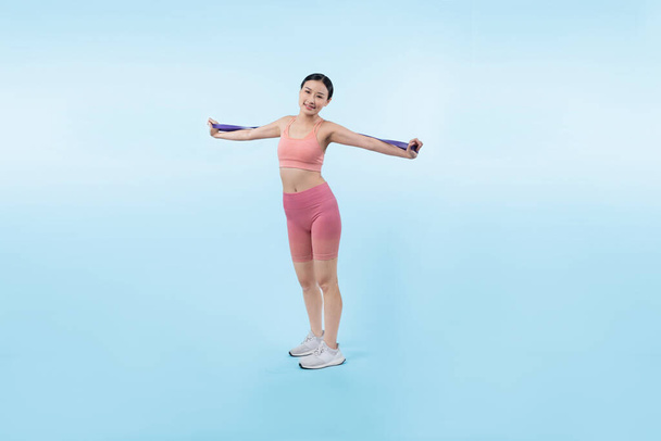 Energiczna kobieta w sportowym portrecie rozciągającym sportową opaskę oporową. Młoda atletyczna azjatycka kobieta siła i wytrzymałość sesji treningowej rutynowa koncepcja treningu na odizolowanym tle. - Zdjęcie, obraz