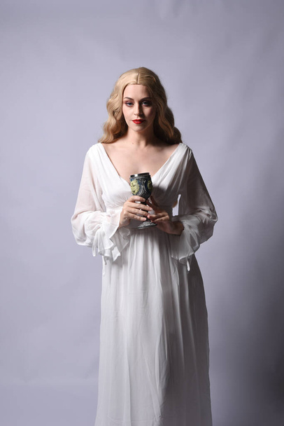 Крупный план портрет красивой блондинки модели носить элегантное белое платье Хэллоуин, исторический фантазии характер. Держа бокал вина, изолированные на аудио фоне. - Фото, изображение