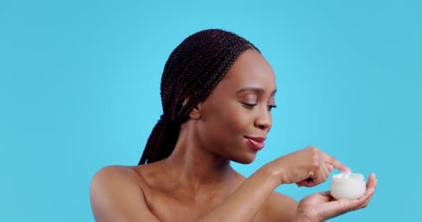 Femme africaine, crème de soin et studio, produit de beauté ou dermatologie pour la santé par fond bleu. Fille, modèle ou sourire avec transformation, lueur ou changement cosmétique avec autosoin pour le bien-être. - Séquence, vidéo