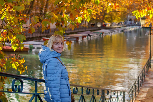 Старша жінка позує по каналу Аннесі з яскравими автентичними деревами, що відображаються у спокійних водах. Старий мандрівник насолоджується мальовничою красою регіону Французьких Альп - Фото, зображення