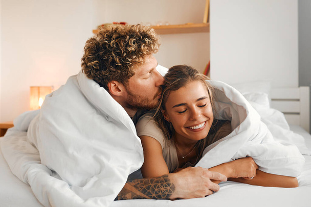 Fiatal pár szerelmes feküdt a kanapén a hálószobában egy takaró alatt, szórakozás és élvezik egymást a hétvégén. - Fotó, kép