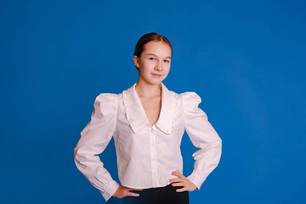 headshot uśmiechnięta nastolatka dziewczyna w białej koszuli patrząc na aparat odizolowany jasnoniebieski studio tło - Zdjęcie, obraz