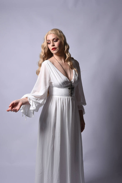 Close-up portret van mooie blonde model dragen elegante witte Halloween jurk, een historische fantasie karakter. Kruis ketting, geïsoleerd op studio achtergrond. - Foto, afbeelding