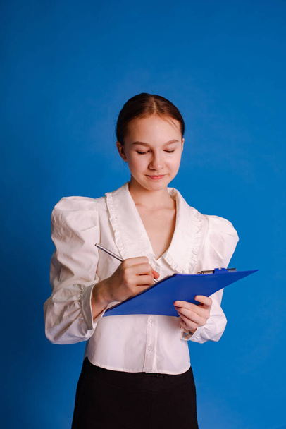 Teenager-Mädchen schreiben Notizen auf Ordner für Papierdokumente isoliert über hellblauem Studiohintergrund - Foto, Bild