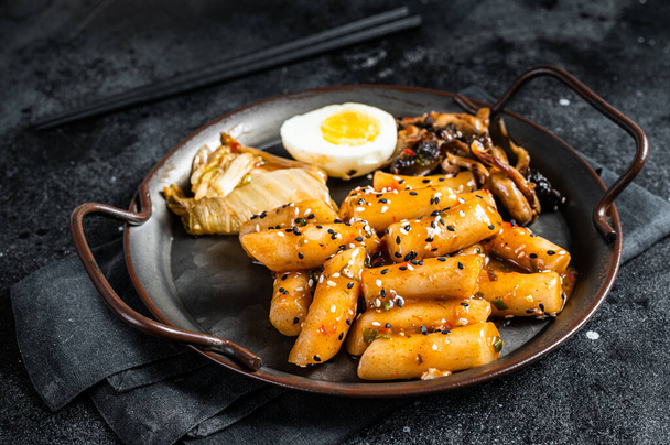 Tteokbokki, Topokki stick rice cake in Hot and spicy sauce with egg and mashrooms. Black background. Top view. - Foto, Bild