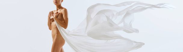 Banner. Cropped portrait of young beautiful naked female body holding on her breast piece of floaty fabric in motion. Concept of natural beauty of body, inspiration, art. Banner. Flyer. Poster. - Фото, зображення