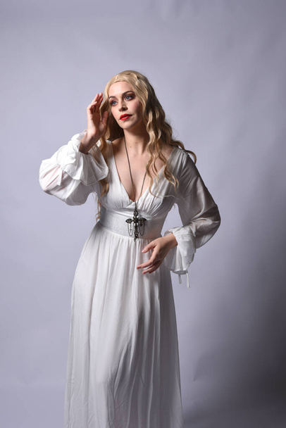 Primer plano retrato de la hermosa modelo rubia con elegante vestido de halloween blanco, un personaje de fantasía histórica. Collar de cruz crucifijo, aislado en el fondo del estudio. - Foto, Imagen