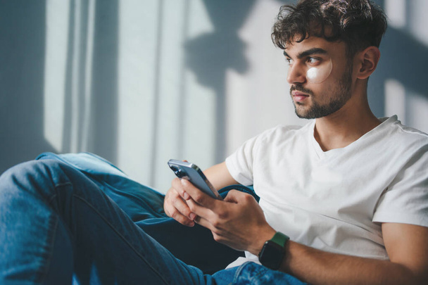 Уверенный бородатый мужчина, сидящий на диване и печатающий на смартфоне, отдыхающий. Домашний образ жизни. - Фото, изображение