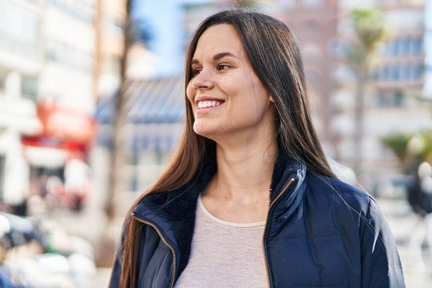 Молода красива іспаномовна жінка посміхається впевнено дивлячись в бік на вулиці
 - Фото, зображення